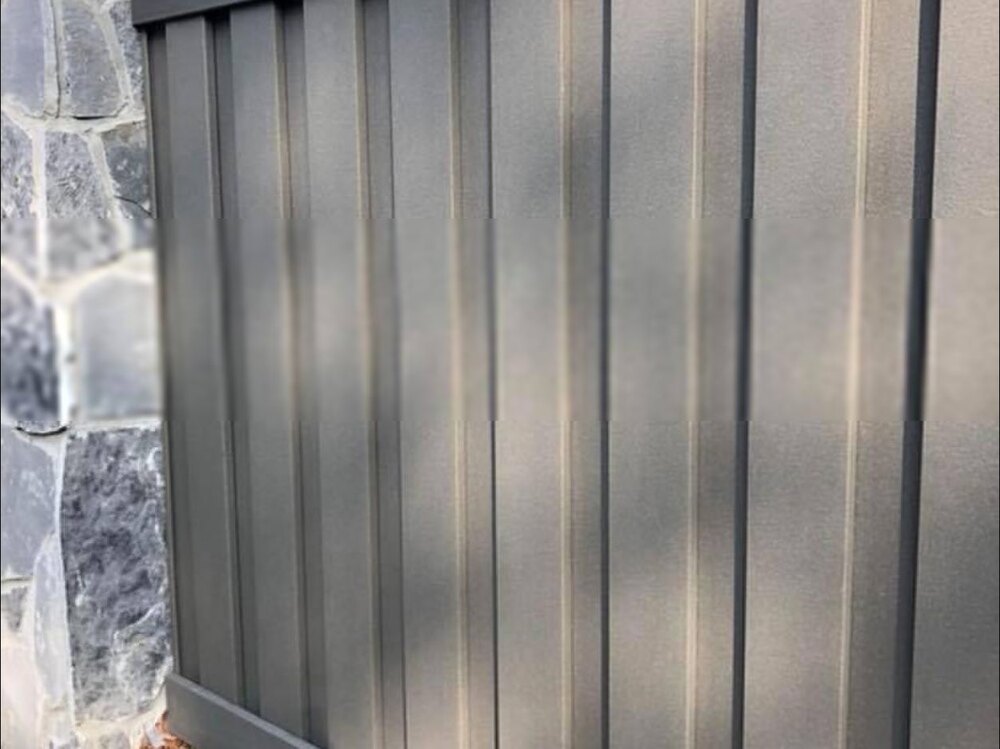 Gray vertical composite privacy fence installed beside a stone column